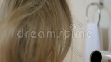 穿着浴巾的漂亮女孩在浴室里用吹风机